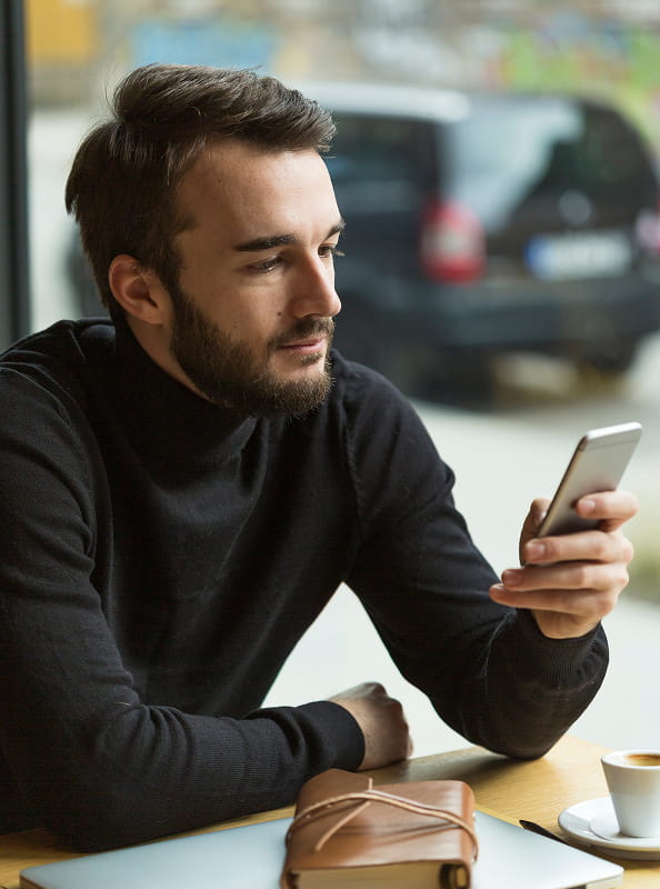 Man using a smartphone in a café, illustrating digital telecommunications customer services.