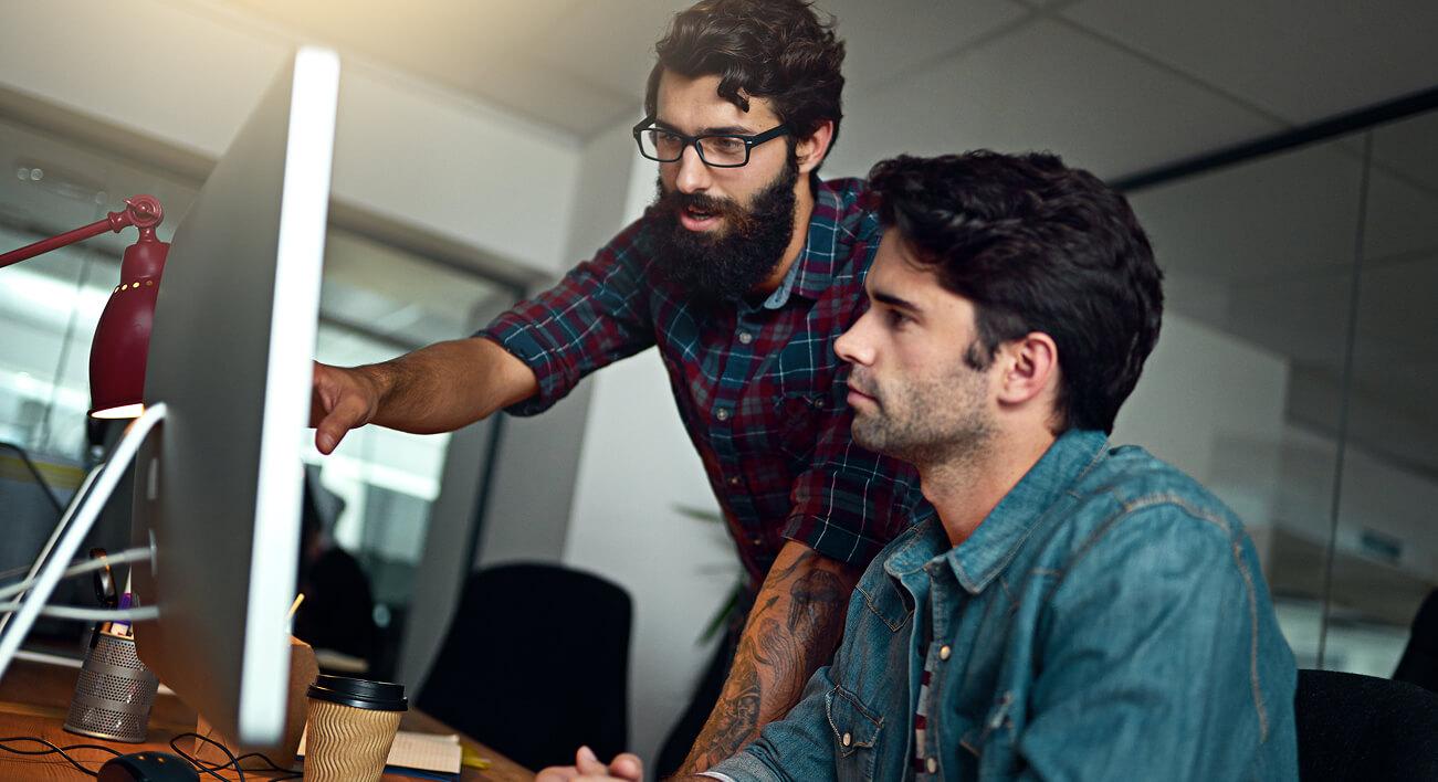 Two colleagues reviewing information together on a desktop computer.