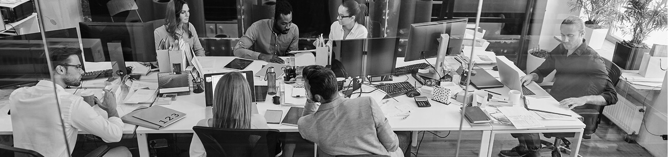 Black-and-white overhead photograph of colleagues working at desks in an open-plan office.