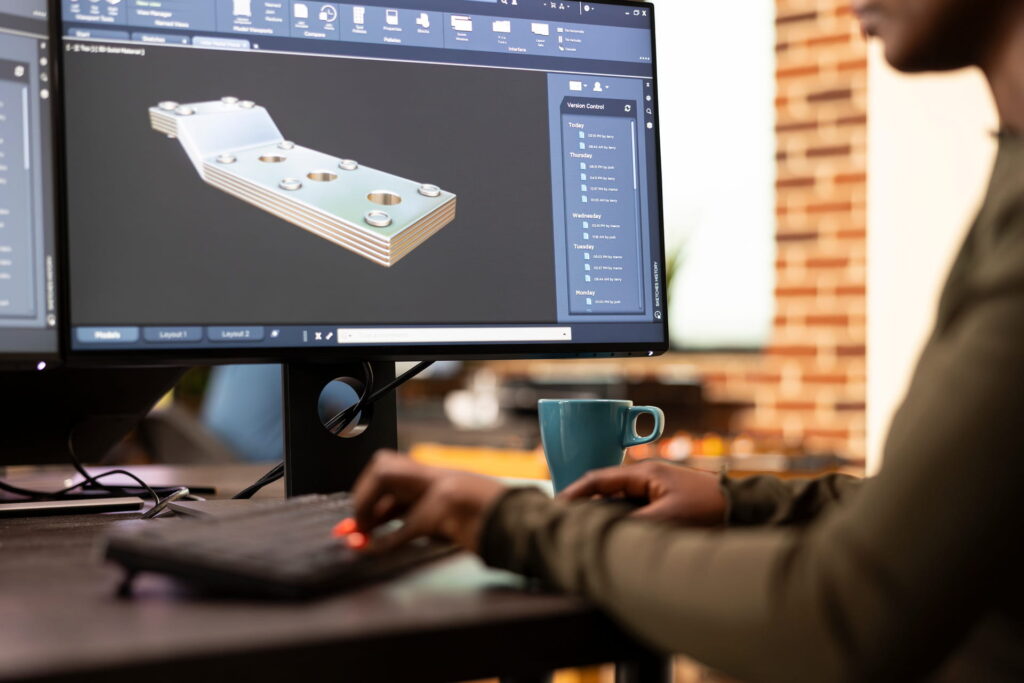 Engineer working with 3D mechanical design software on a desktop monitor.