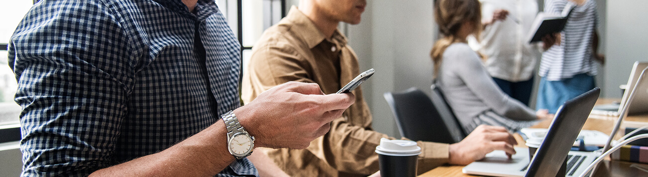 Professionals using a smartphone and laptops while working together in a shared office.
