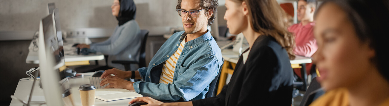 Colleagues discussing work at desktop computers in a modern office.